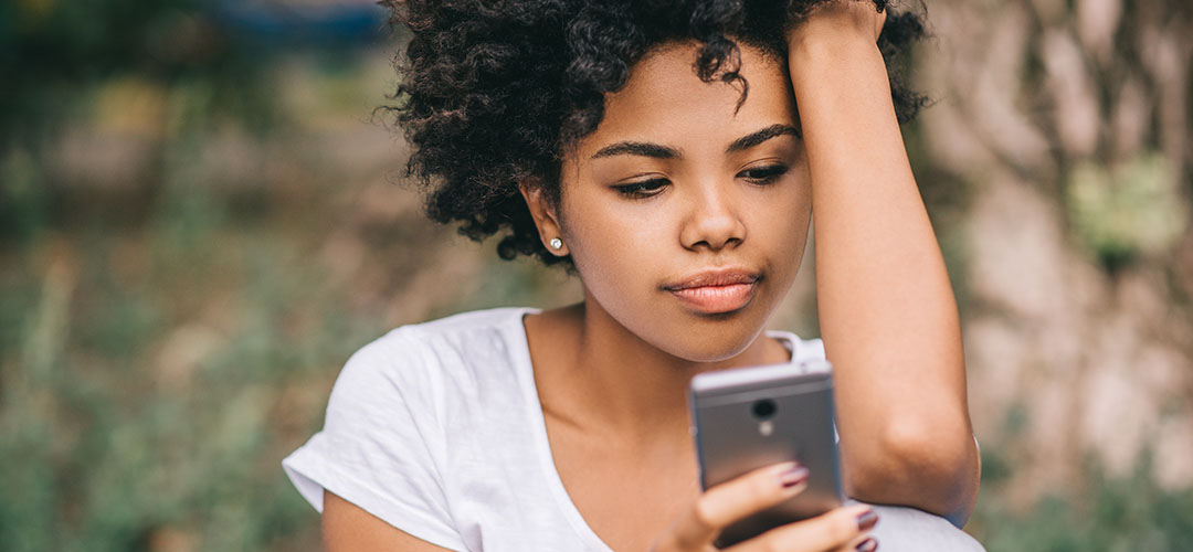 Beautiful African American Female Student Sitting On Bench reading her cell phone