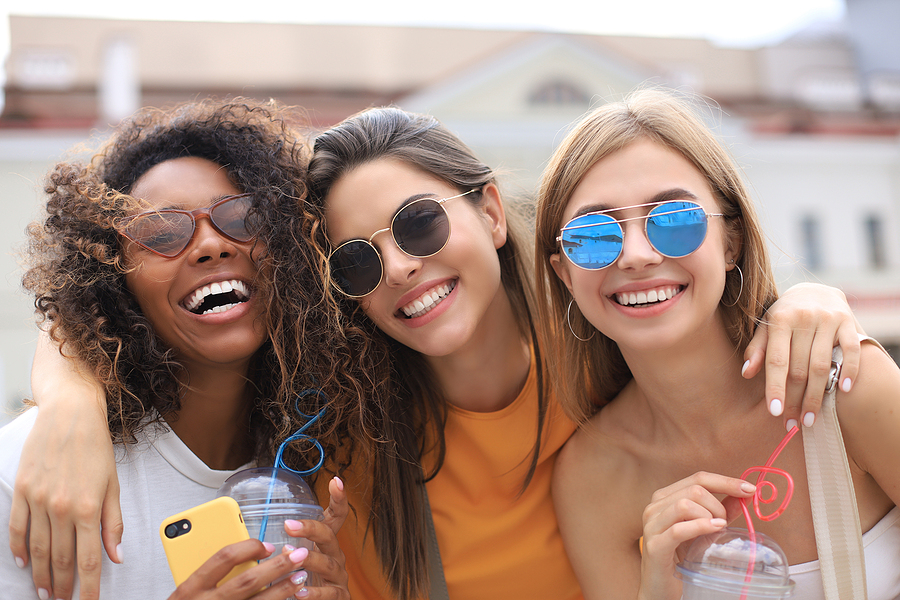 Three trendy cool hipster girls, friends drink cocktail in urban city background.